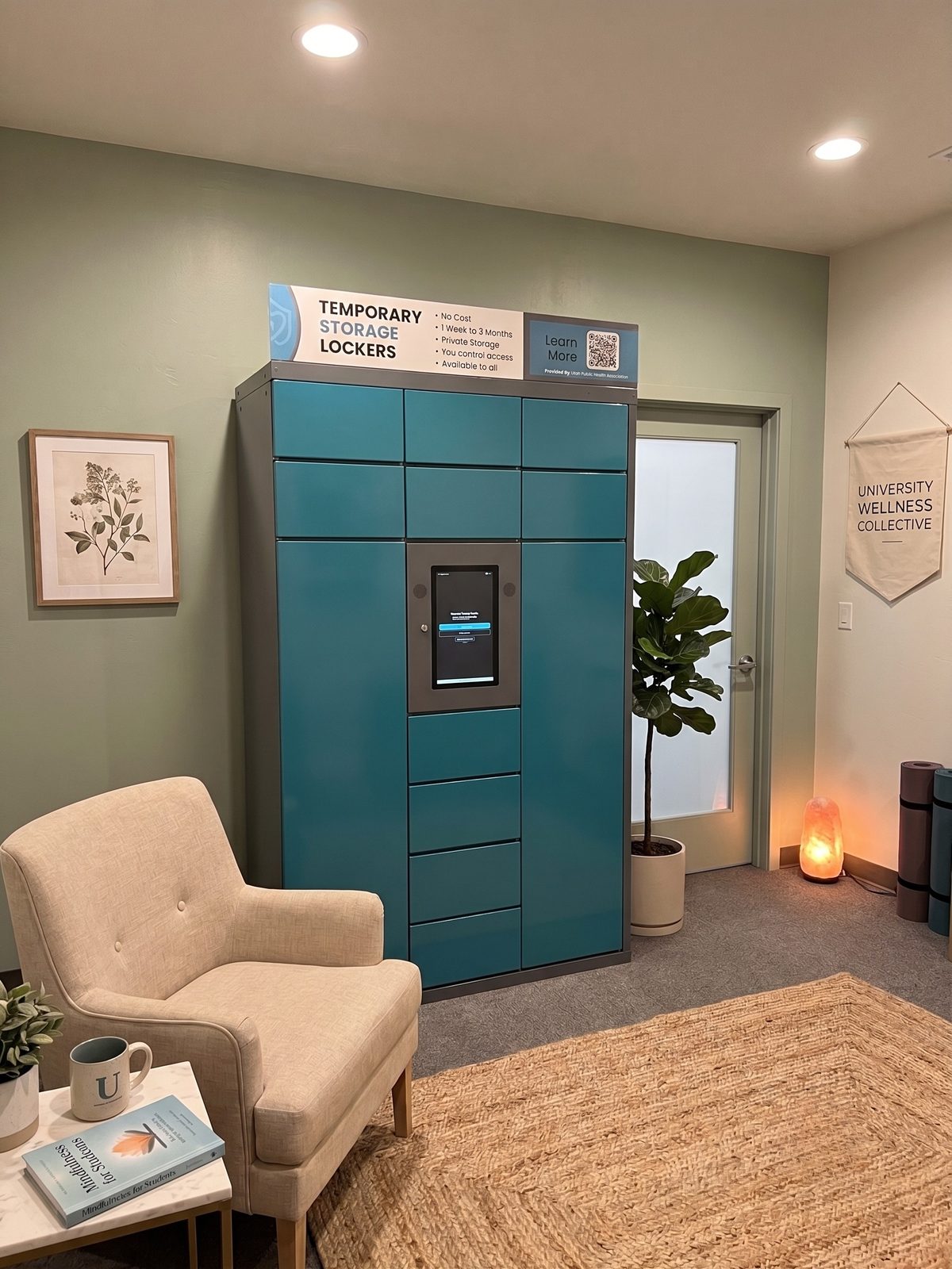 A bank of teal SafeReach temporary storage lockers with a touchscreen kiosk, installed in a university wellness centre next to an armchair and a plant.