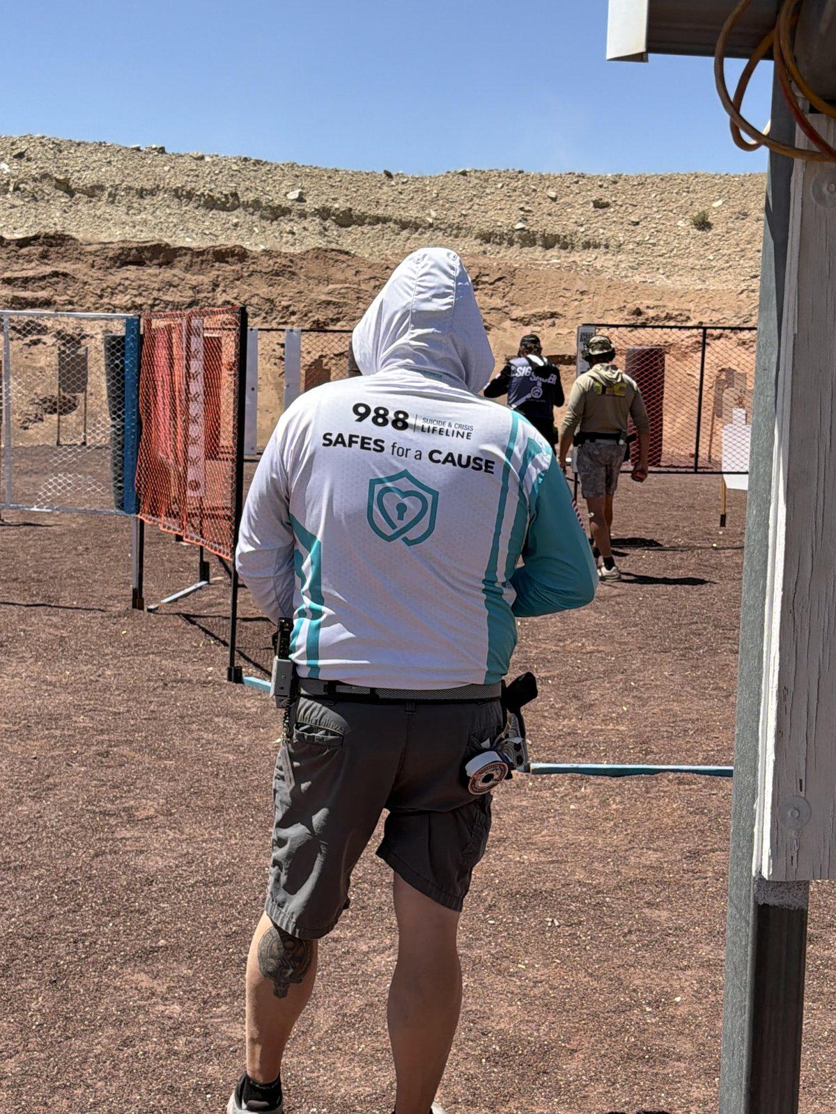 A member of the SafeReach competitive shooting team on a range, wearing a team jersey printed with the 988 Suicide and Crisis Lifeline and the Safes for a Cause logo.